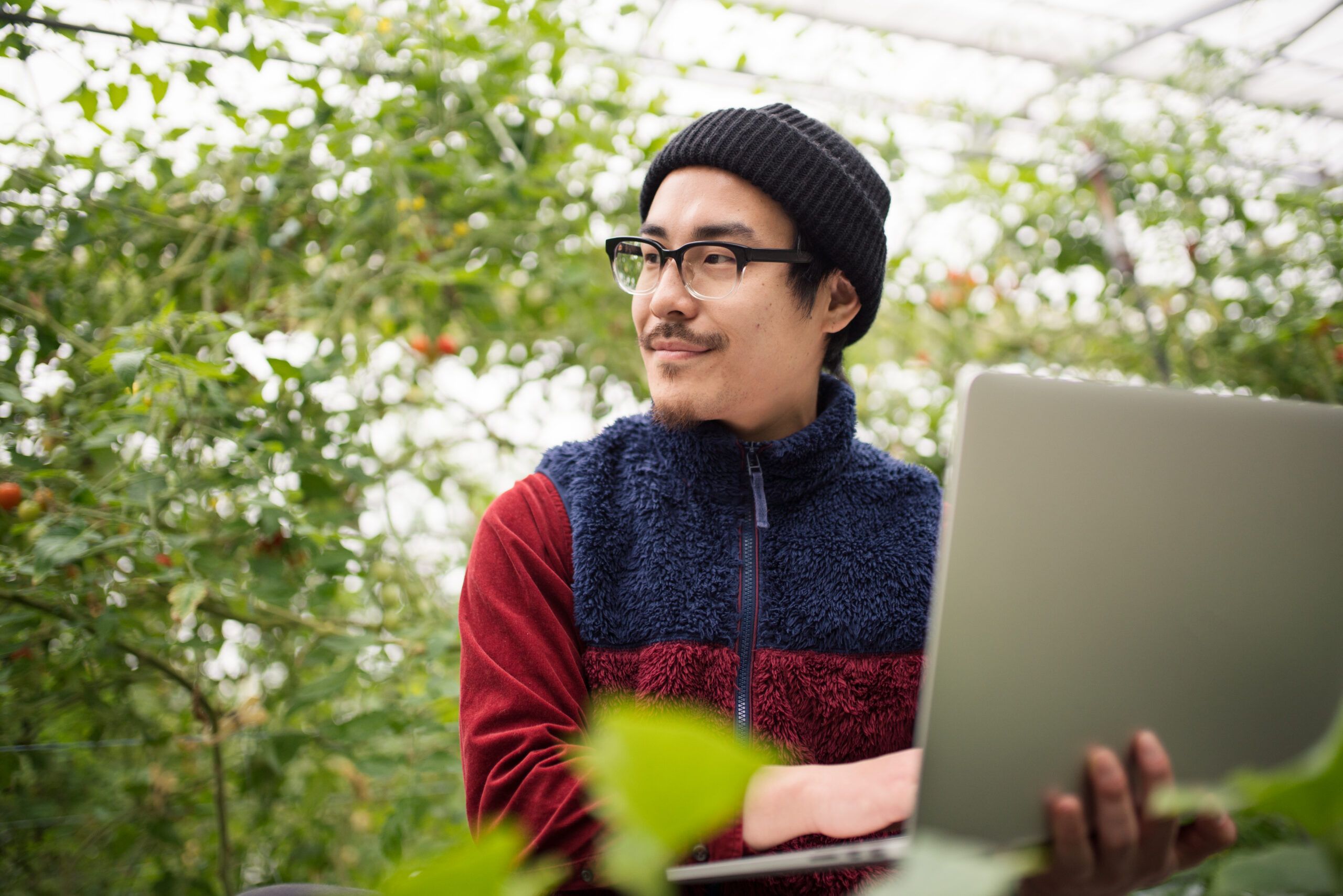Young male farmer with a laptop computer in a greenhouse conducting research. Okayama, Japan. March 2016
