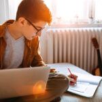 一个十几岁的男孩写的笔记本电脑在他的膝盖上。