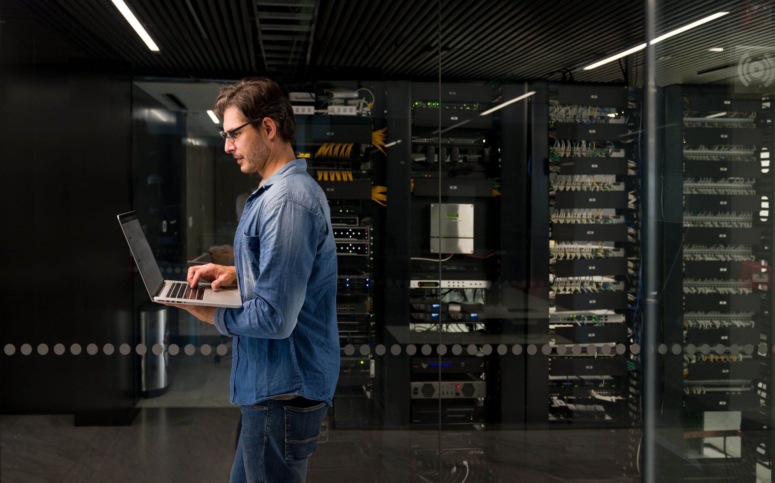 A person walking through a server room whilst using a laptop.