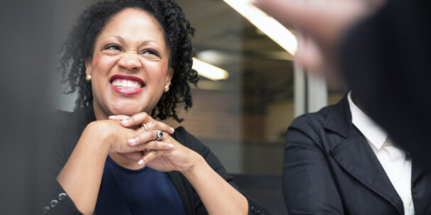 Woman sits at a table and leans on her hands, smiling
