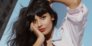 Jameela Jamil looks to camera with head resting on one hand, the other hand is on top of her head