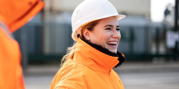 A female engineer wearing a hard hat laughs with colleagues
