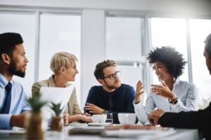 A group of professionals seated a table in an office looking at a colleague who is speaking.
