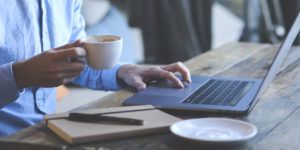 A man using a laptop with coffee and a notebook
