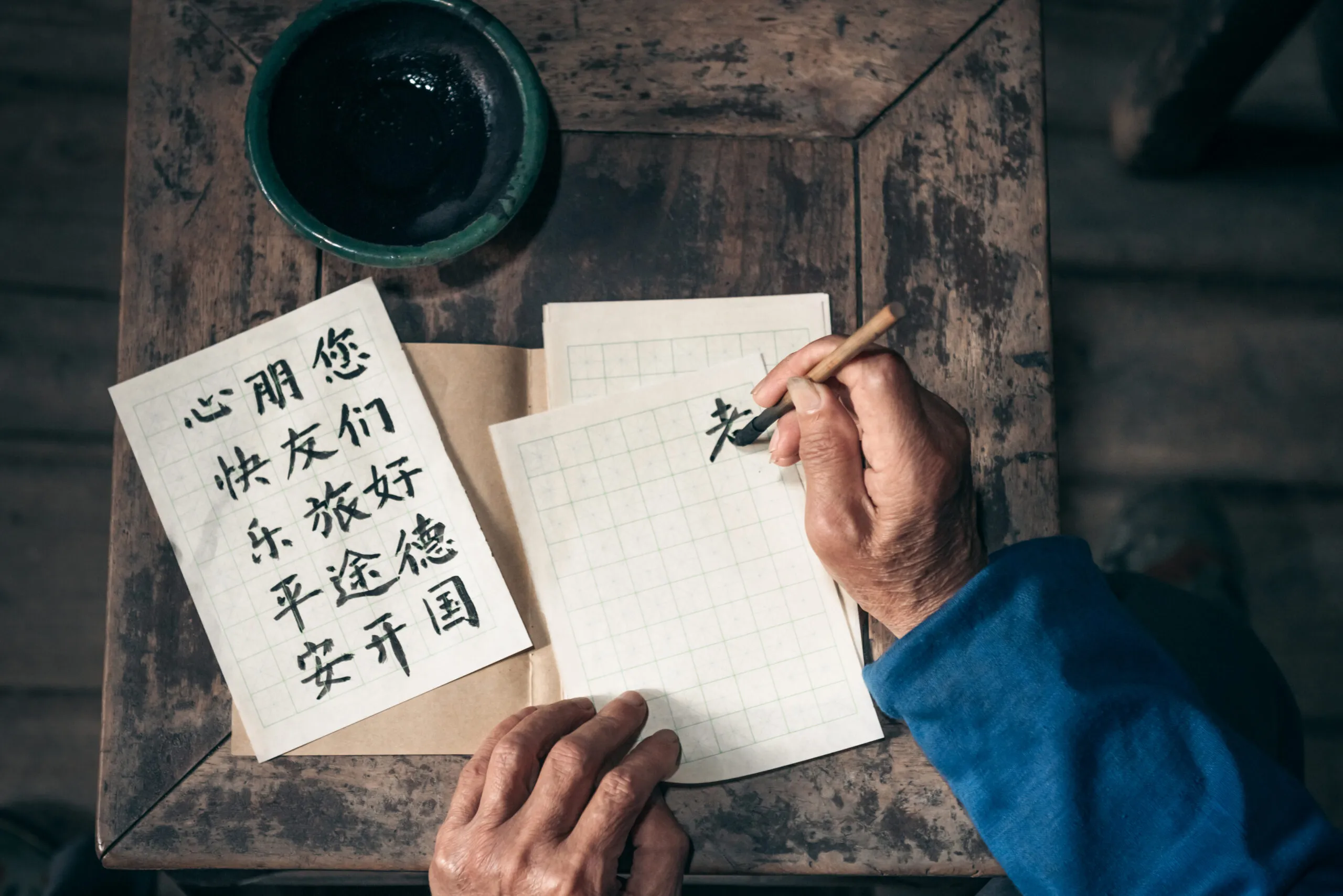 From above, two hands painting Kanji calligraphy.