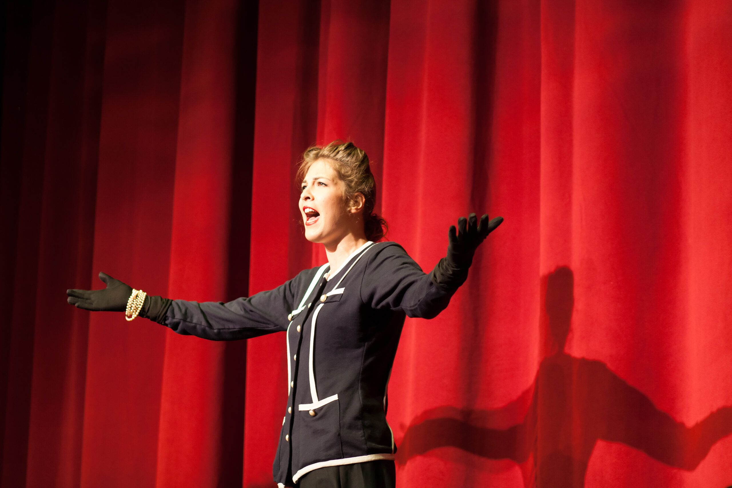 Individual standing on a stage with their arms spread wide and mouth open.
