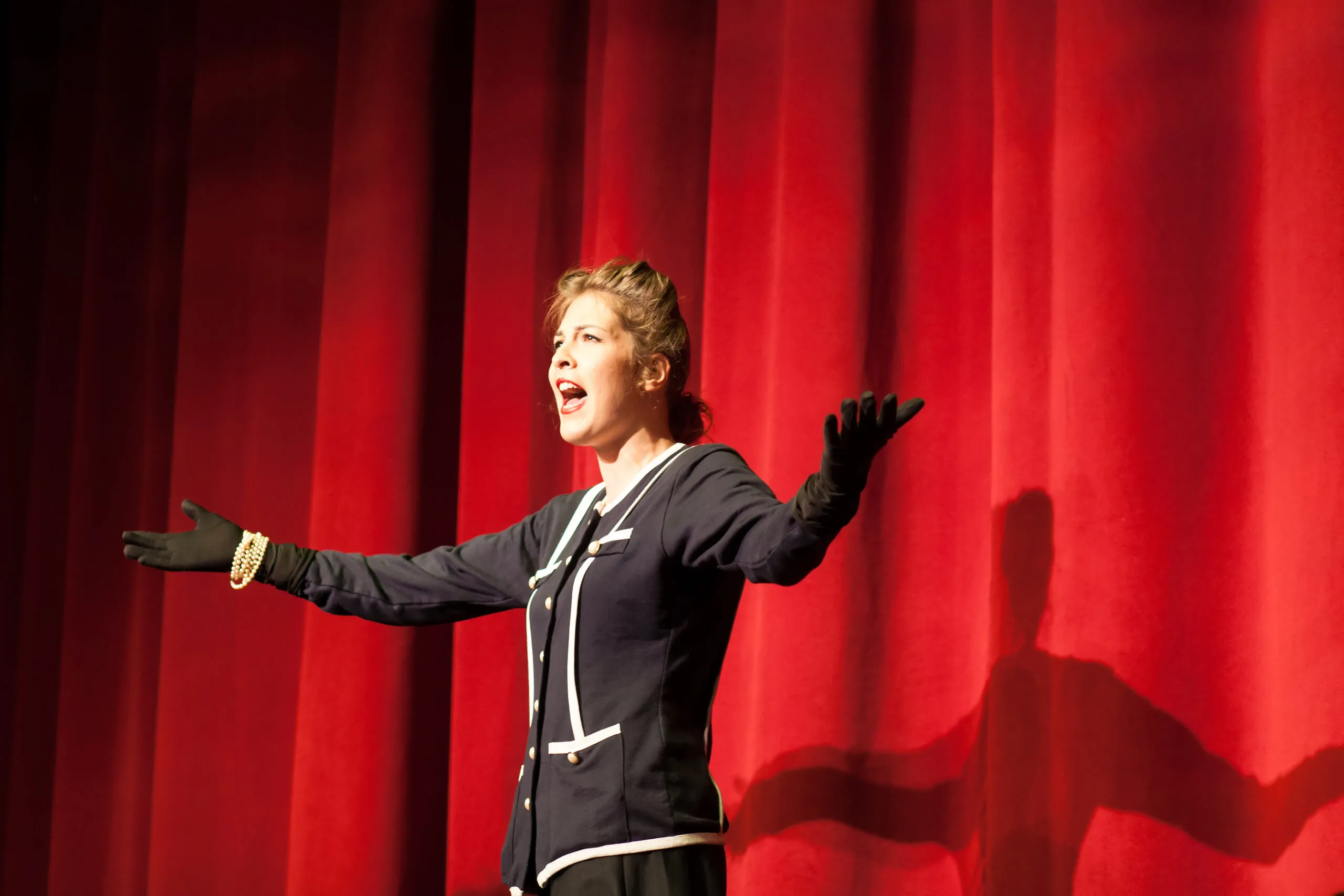 Individual standing on a stage with their arms spread wide and mouth open.